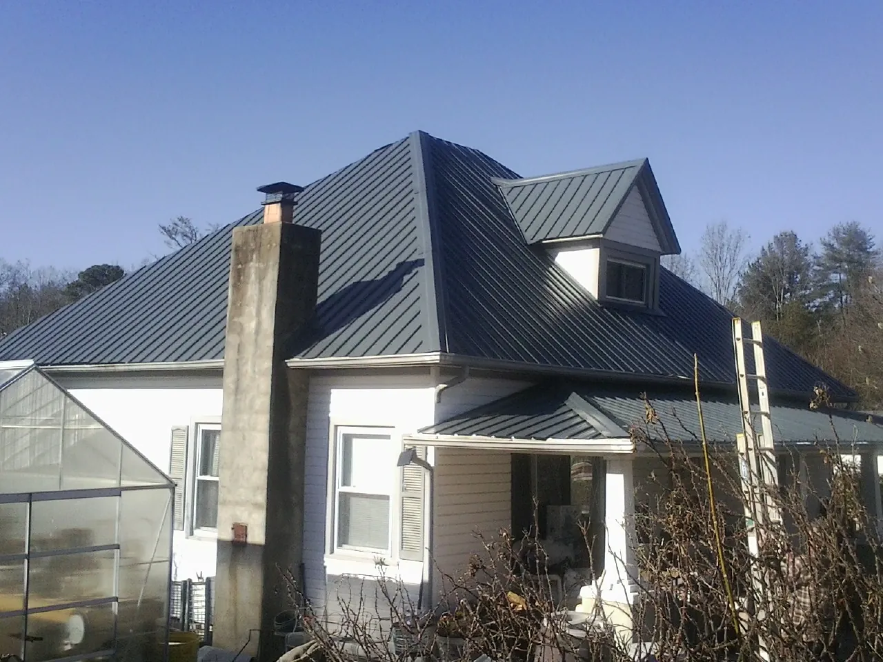 Dark blue standing seam metal roof on a white farmhouse with dormer — Slate & Tile Roof Repair by Roofing Brothers in Fentress