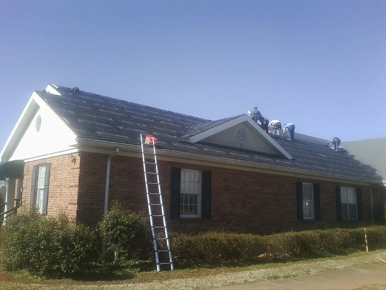 Crew tearing shingles off a brick ranch roof with a ladder set — Emergency Roof Repair work by our crew in Fentress