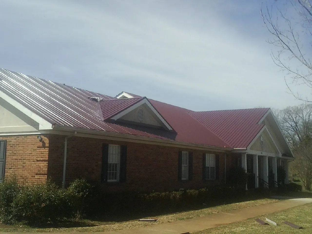 Red metal roof with gabled entries on a long brick building, from a Hail Damage Roof Repair job in Fentress