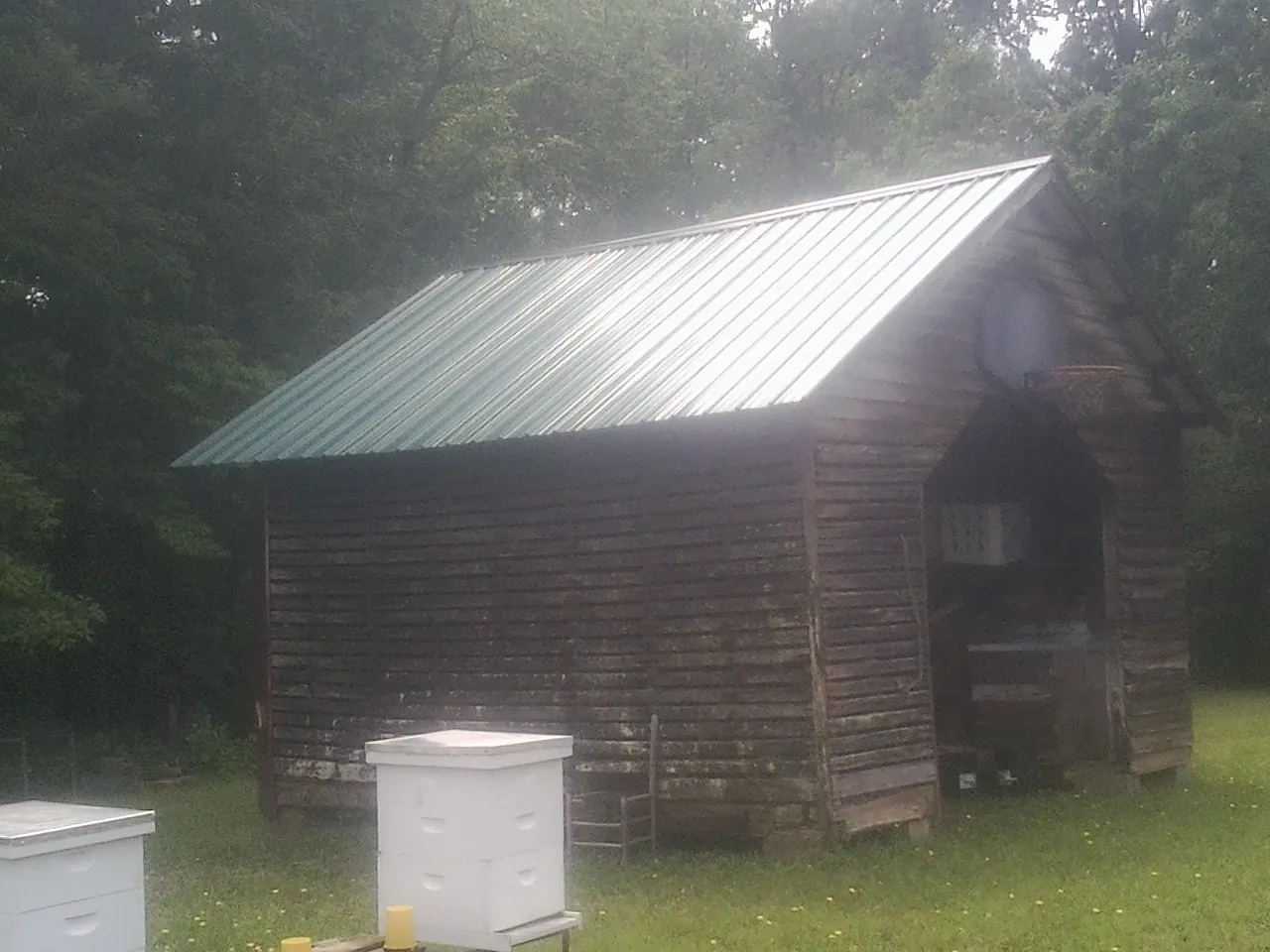 Green metal roof on a weathered barn beside stacked beehives in Fentress