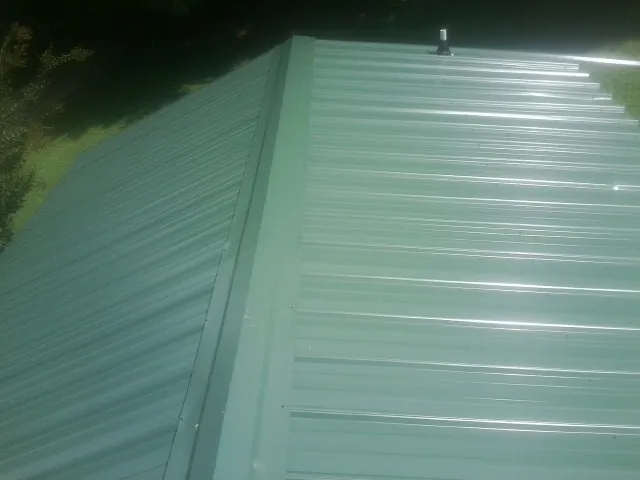 New green metal panels meeting at the ridge of a roof — Flat Roof Repair work by our crew in Fentress
