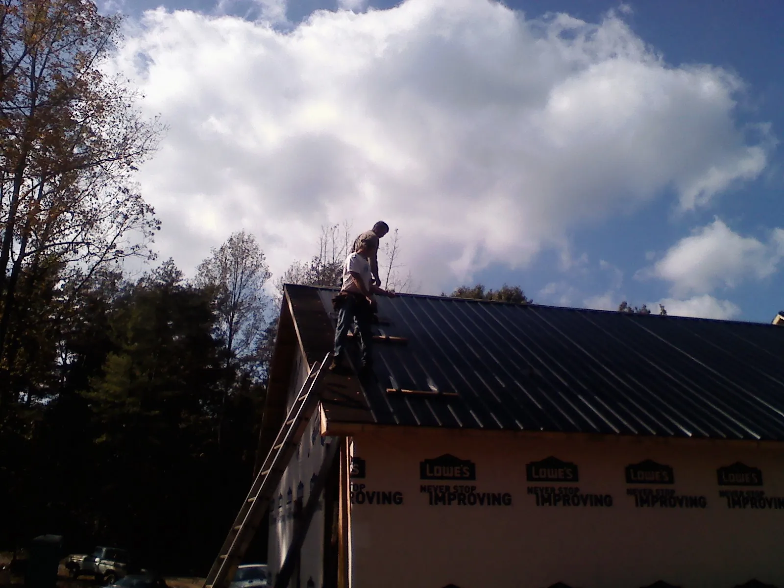 Roofer fastening dark metal panels high against a cloudy sky, from a Roof Inspection job in Fentress