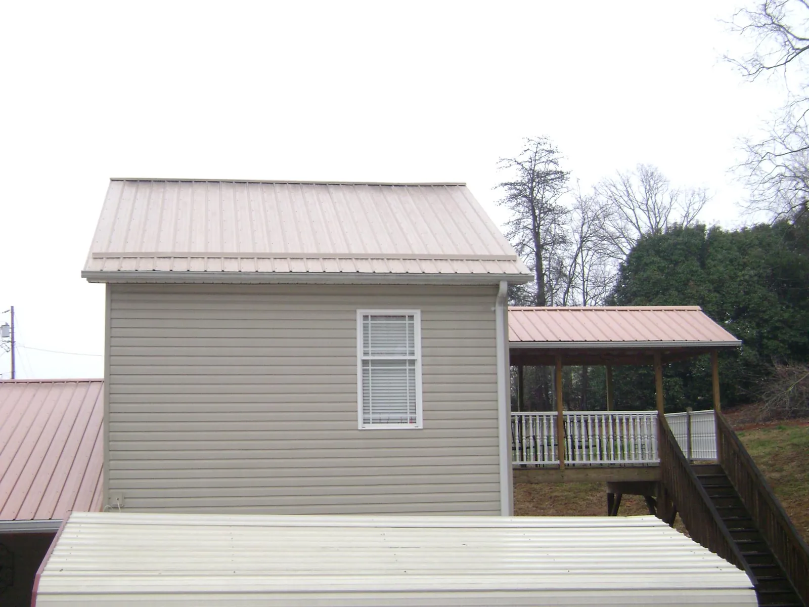 Tan metal roofs on a two story addition and attached porch, from a Roof Replacement job in Fentress